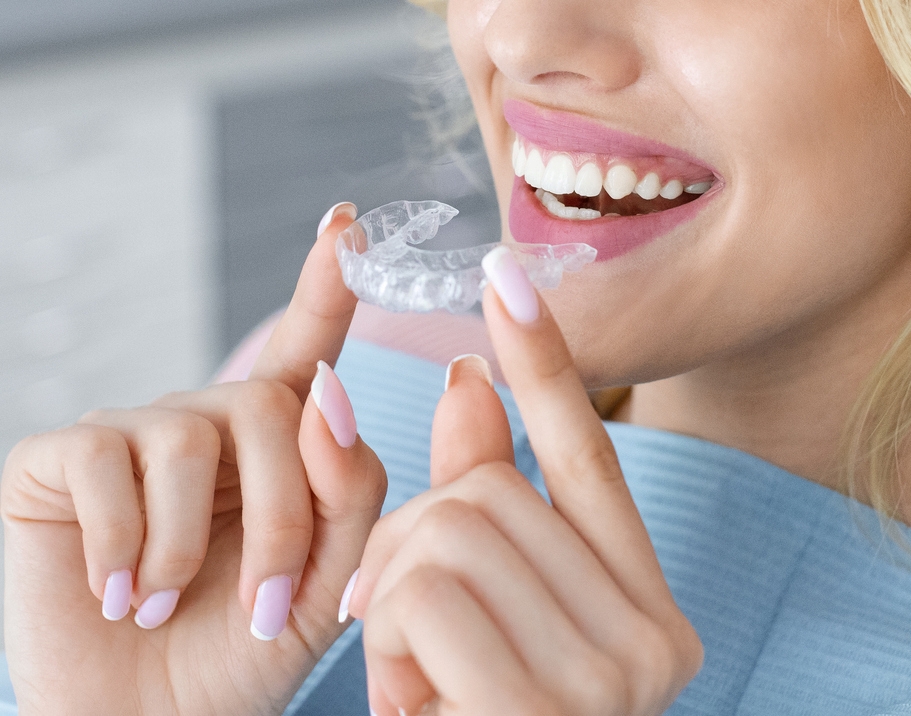 smiling woman holding clear aligners near her mouth.